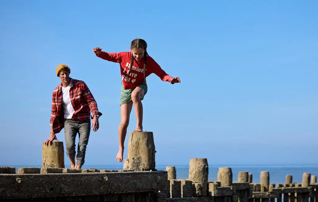 Adult man and 10-year-old girl climb on the pier by the beach in Norfolk.