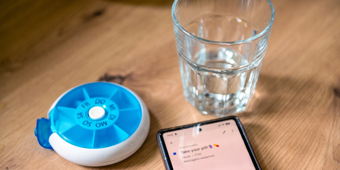 Phone with a reminder on daily medication, a pill box, and a glass of water