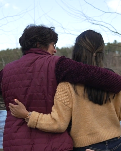 Two women with their arms around each other looking out at water