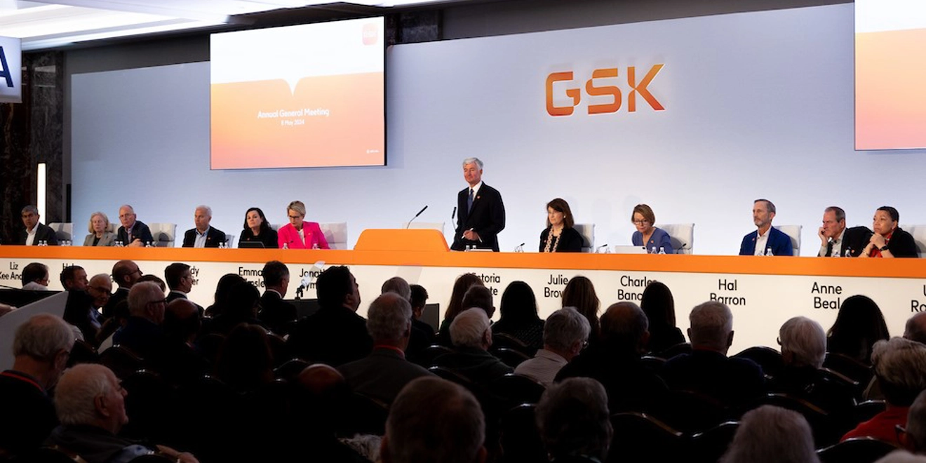 GSK Board on stage at AGM 2024, Jon Symonds speaks at podium, audience listens